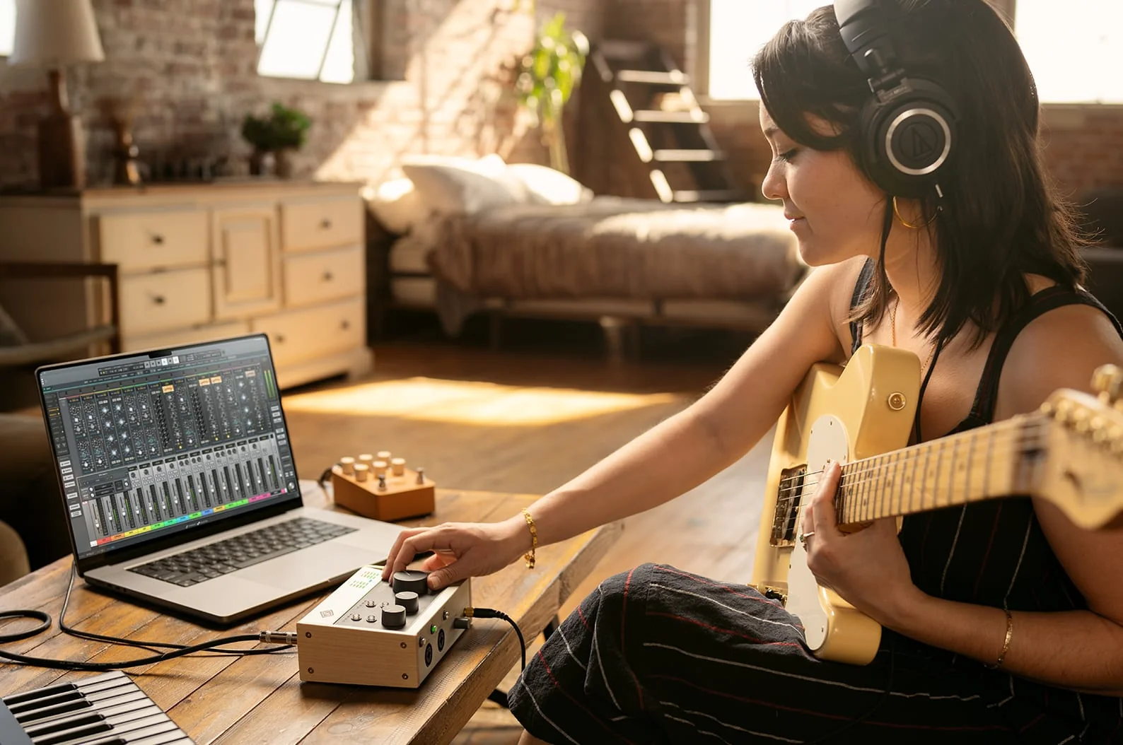 Produtora criando com guitarra, laptop e controlador no chão da sala